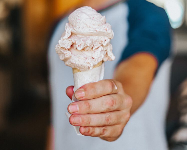 Man holds a cone with two scoops of strawberry ice cream as it starts to melt down the right side of the cone.
