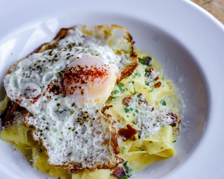 Sunny side egg tops fresh semolina pasta and covered in finely grated parmesan cheese