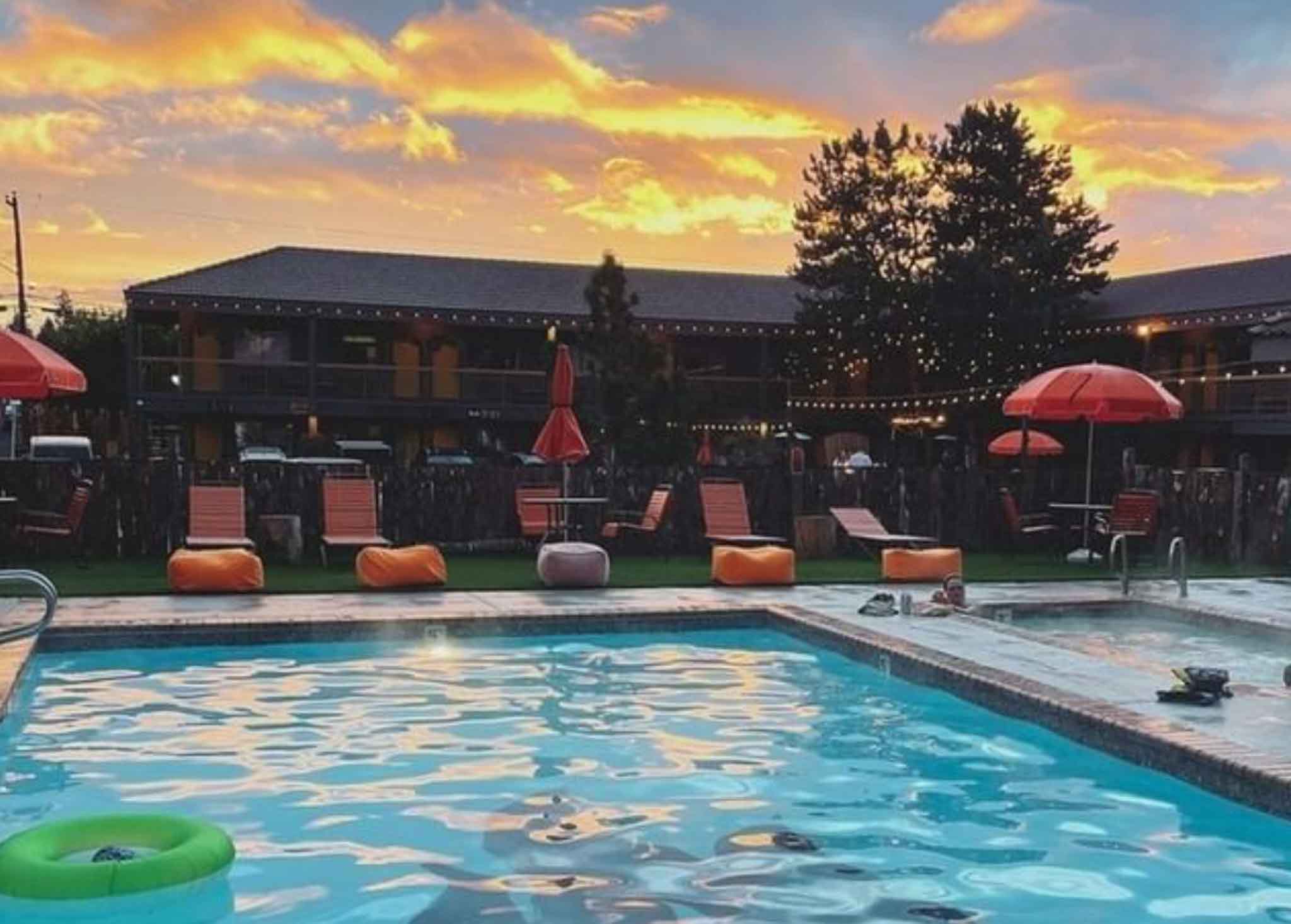 sun sets over a summer sky and pool lined with orange chairs and umbrellas
