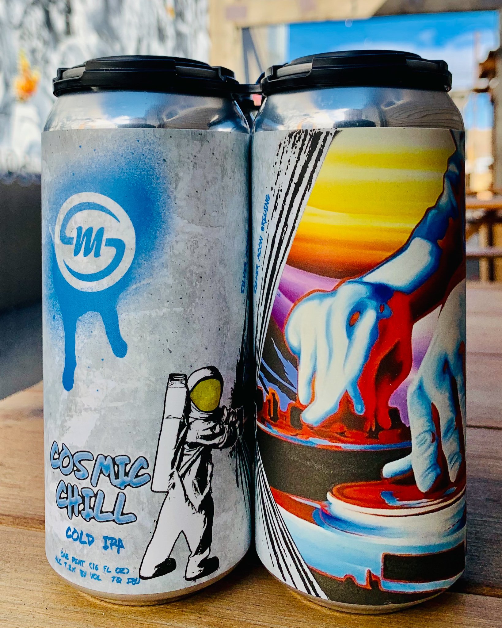 Two tall beer cans of silver moon cosmic chill feature spray painted bright colored art including a man in space suit