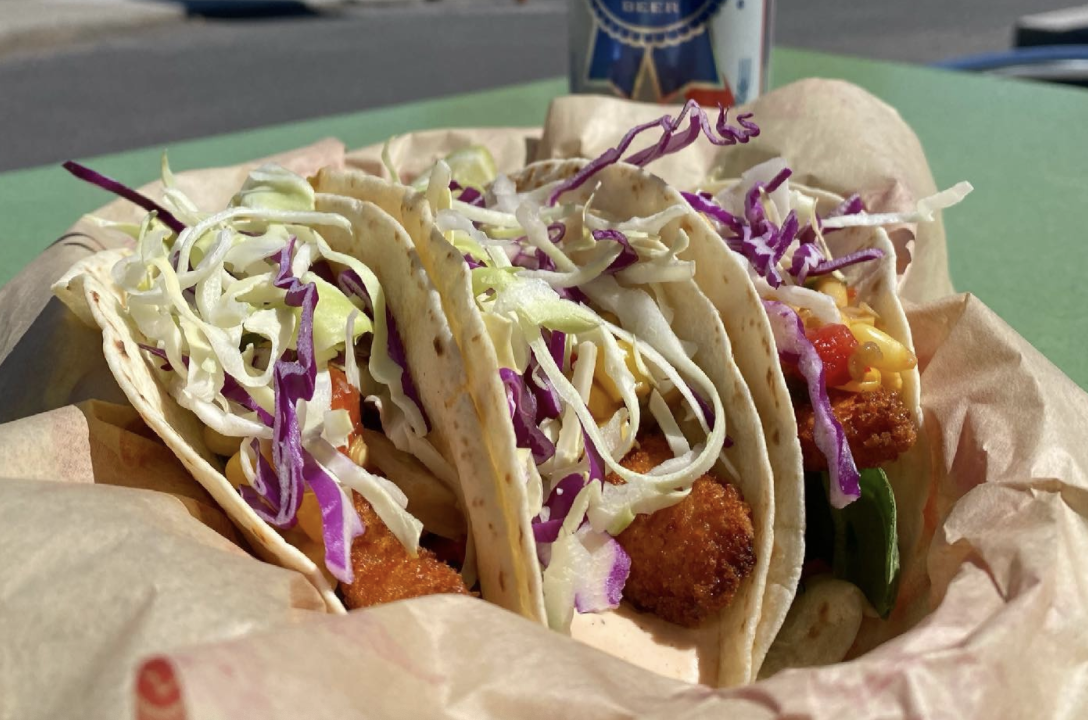 three flour tortilla tacos in a basket filled with fried fish, cabbage slaw, and dressing at parilla grill.
