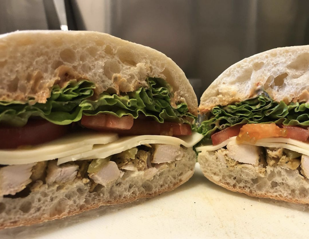 White bread roll sandwich is cut in half to show of the chipotle diced chicken, sliced cheese, tomatoes, and leaves of lettuce.