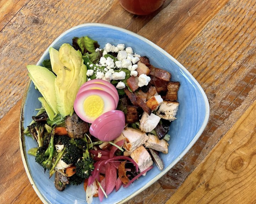 OVERHEAD view of pale blue plate holding a salad of lettuce, avocado, bleu cheese crumbles, hard boiled egg, and pickled onions.