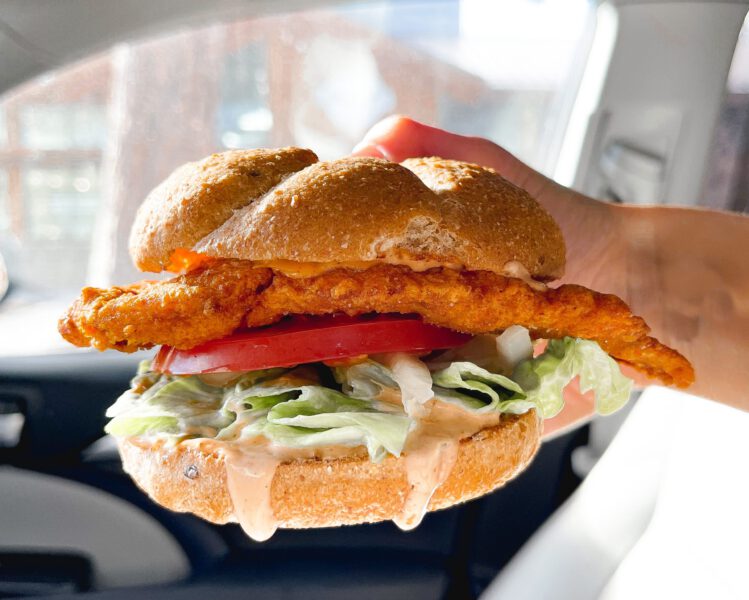 Hand holds a crispy chicken sandwich with hot sauce dripping from the bottom of the bun to showcase quick weekday lunch in bend oregon