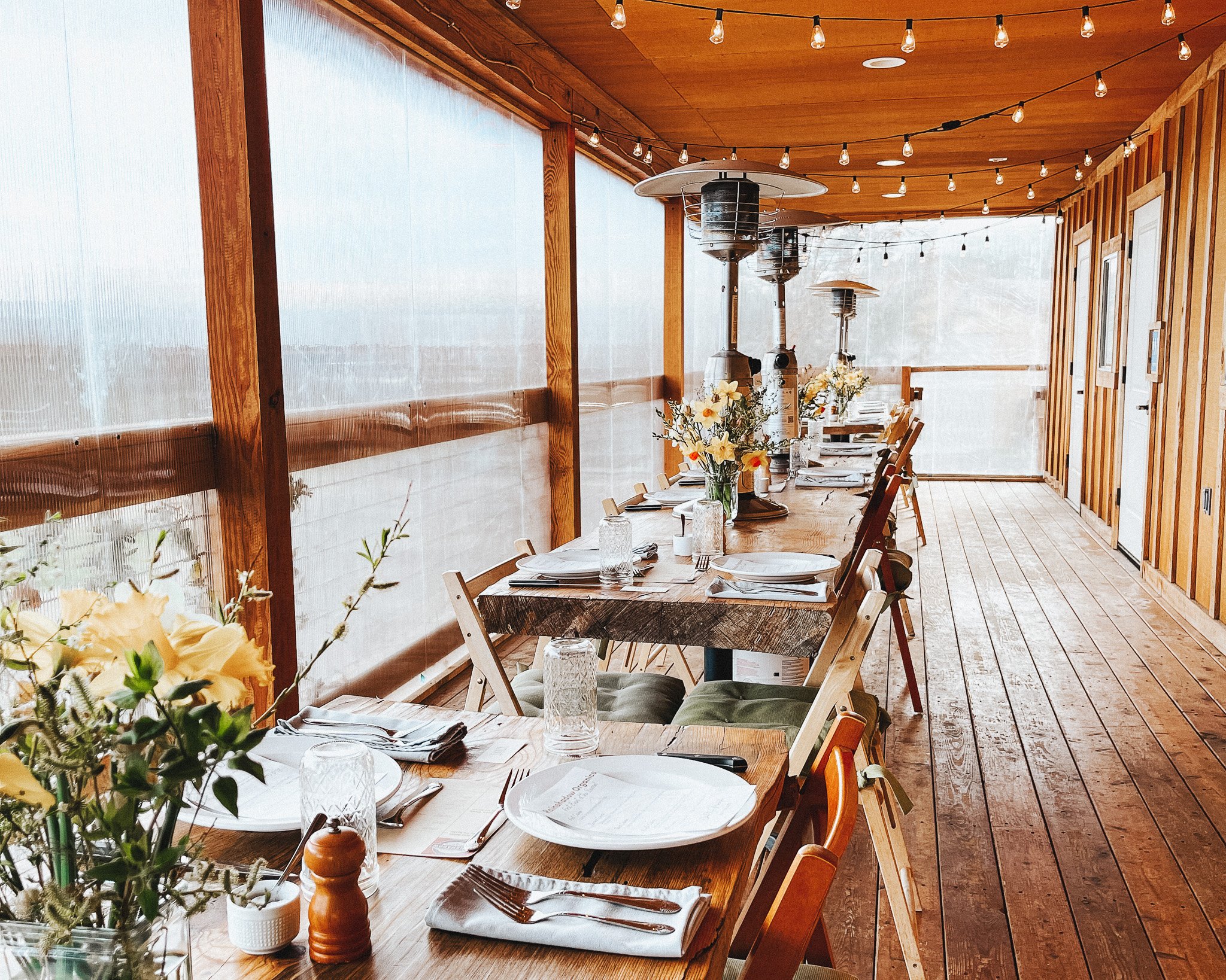 tables along a deck with plates, flowers, string lights and heat lamps