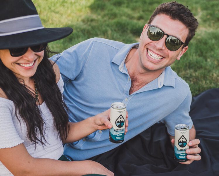 man and woman hold a can of altitude beverages cold brew while smiling at the camera
