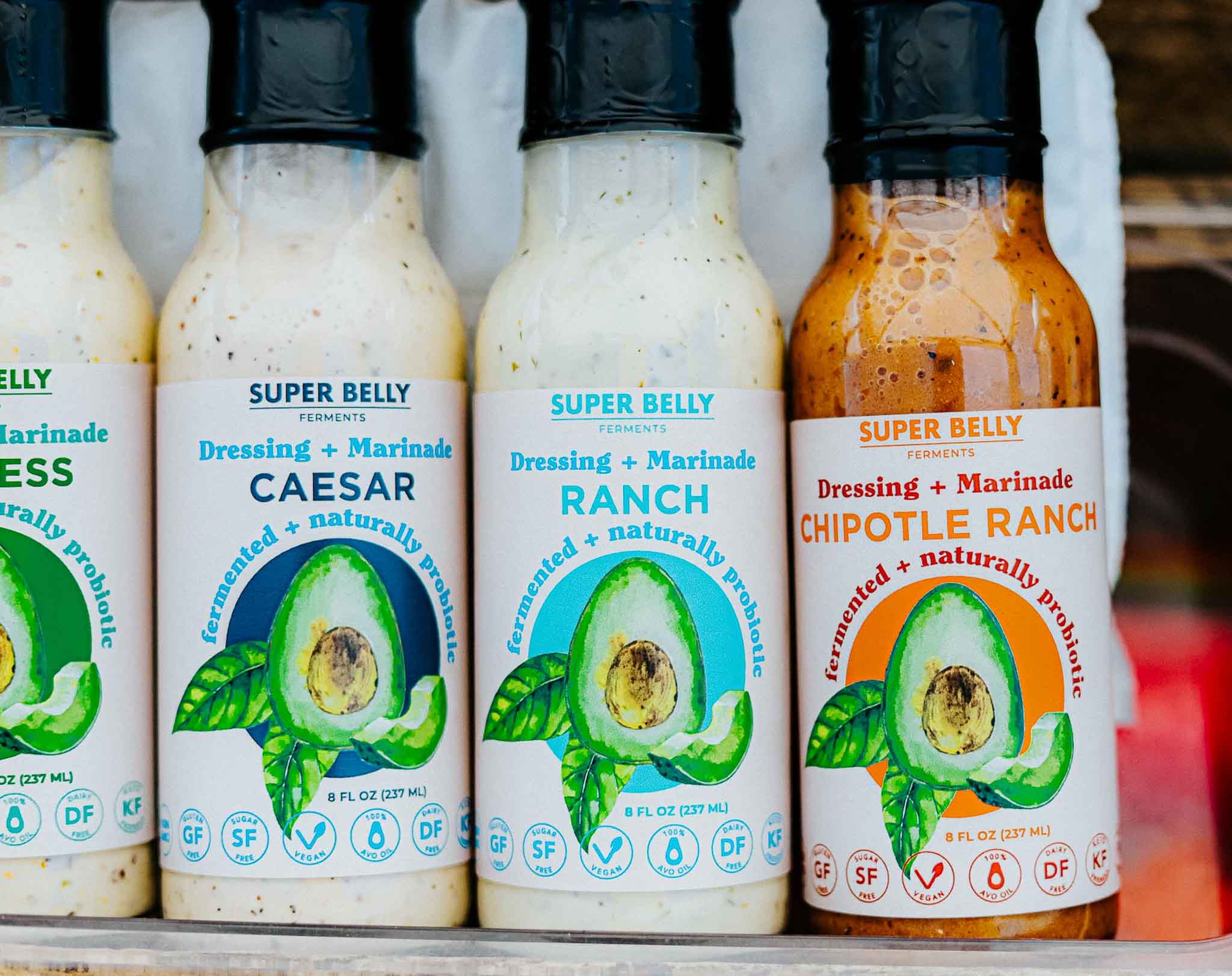 row of salad dressing bottles labled "super belly ferments" with an avocado logo on the front