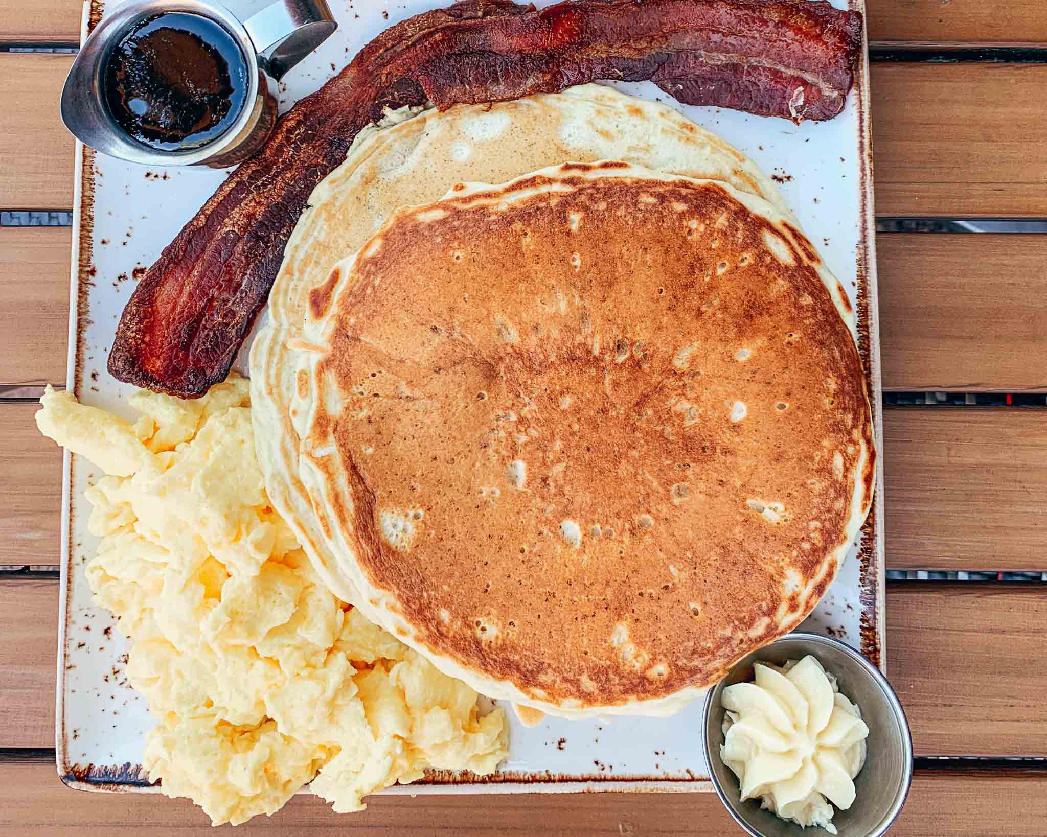 Overhead view of plate with pancakes, scrambled eggs, and a crispy slice of bacon