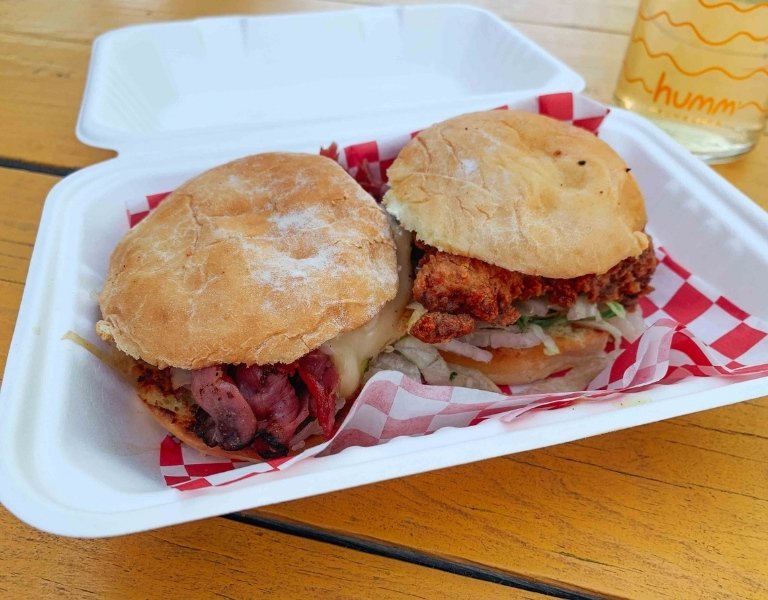two sliders with spicy fried chicken sit in a white to go box lined with red and white checkered paper