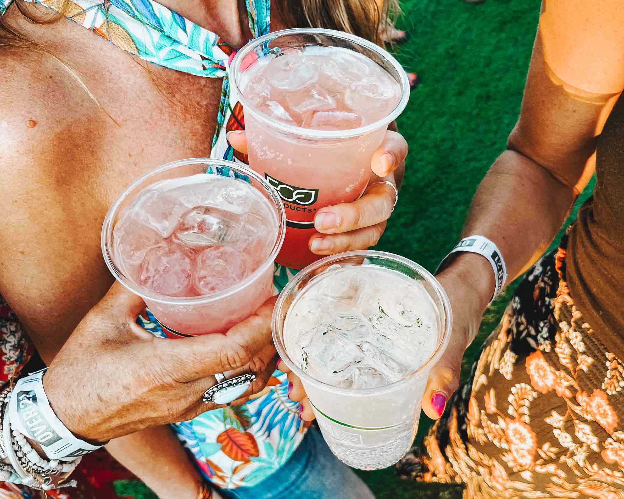 Three hands cheers clear cups with ice and drinks while attending Bend concerts