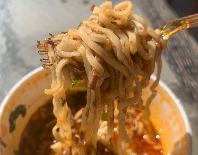 fork pulls ramen noodles from a bowl of birria and consome