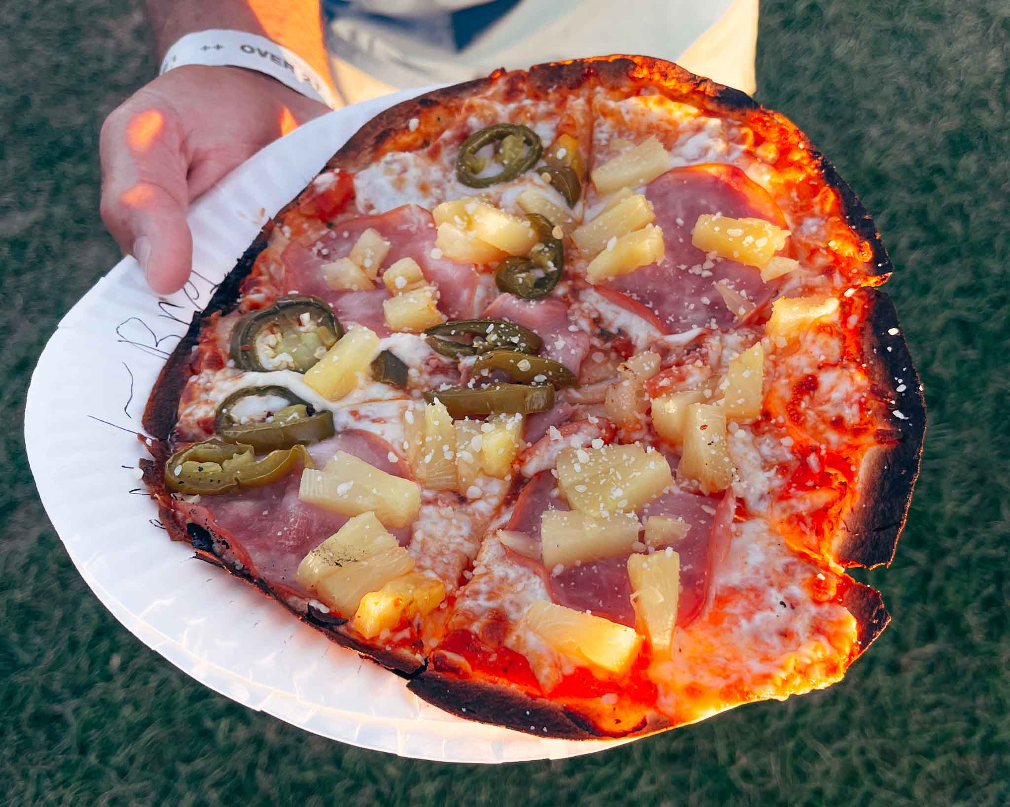 Hand holds a plate of pizza with jalapenos and pineapple at Bend concerts