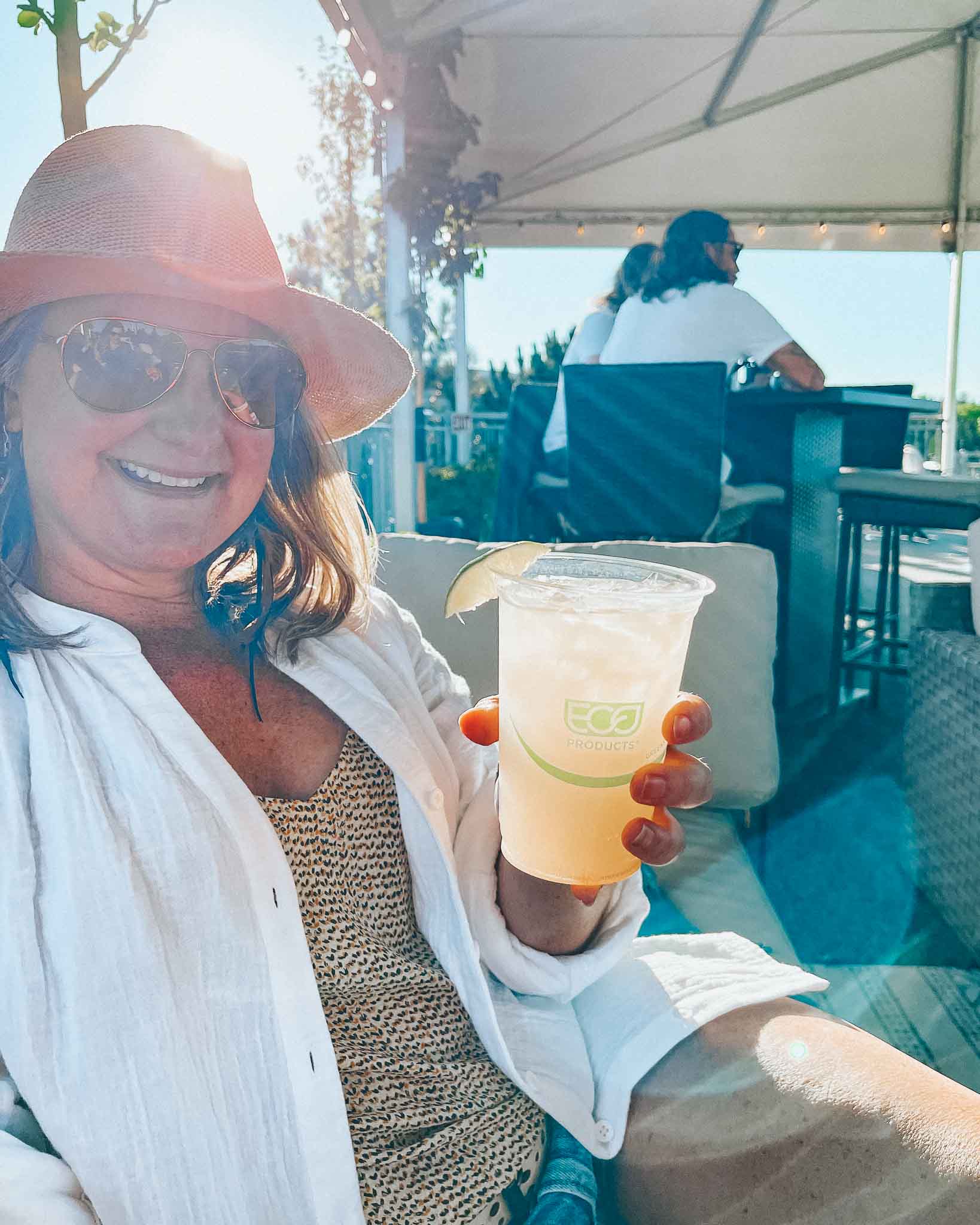 Woman holds a margarita while smiling and sitting on a sofa on the deschutes deck at bend concerts