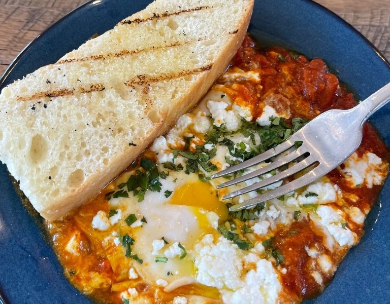 Blue plate of red sauce topped with an egg and slice of bread with grill marks