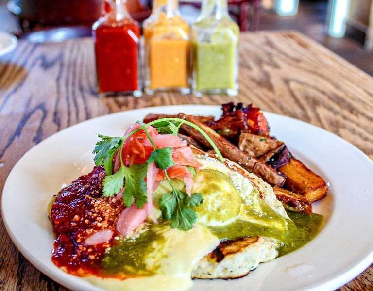 plate of colorful food, including yellow hollandaise, red sauce, green sauce, and cilantro over a cornmeal pancake and top 10 best brunches in bend oregon
