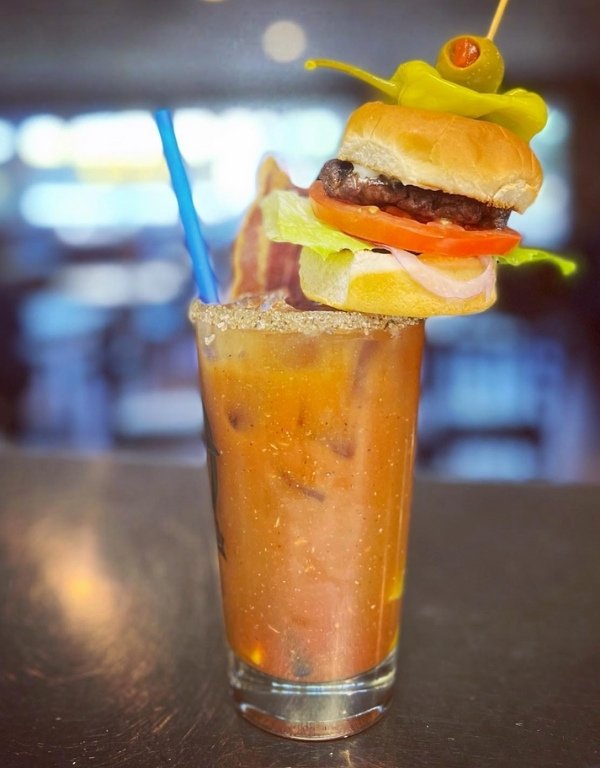 bloody mary in tall glass is skewered with a miniature burger