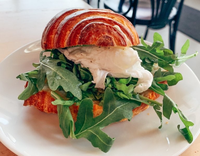 croissant filled with brightly colored arugula and a poached egg on a white plate which is regularly named best brunch in bend oregon