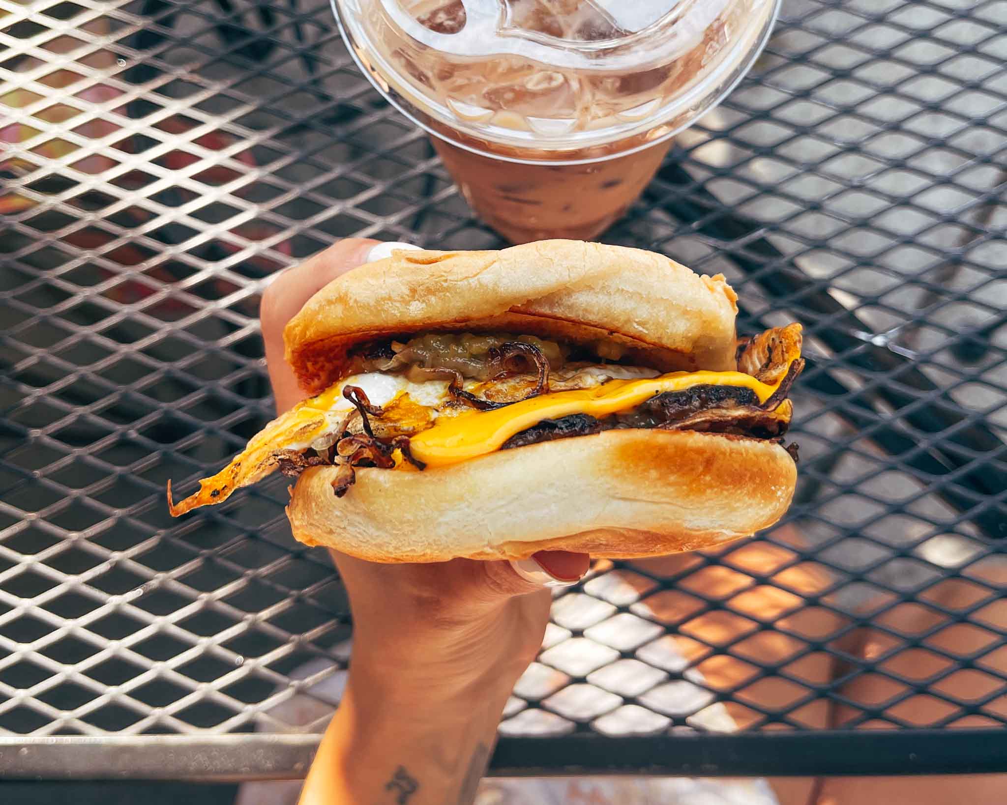 Hand holds a smash burger with fried egg and cheese melting down the patty