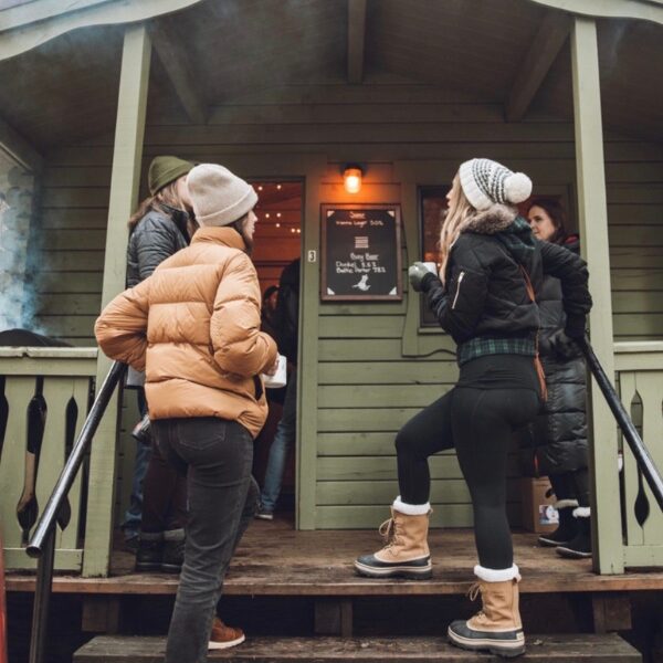 two women stand on the steps of rustic cabins at the suttle lodge winter beer festival