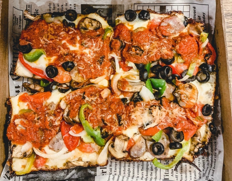 Detroit style pizza from a square pan sits in a pizza box lined with newspaper