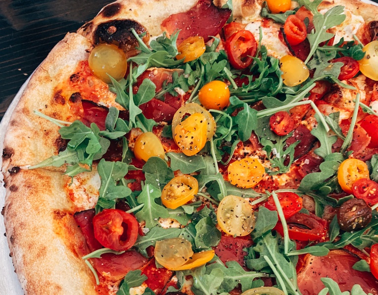 pizza topped with arugula and sliced cherry tomatoes