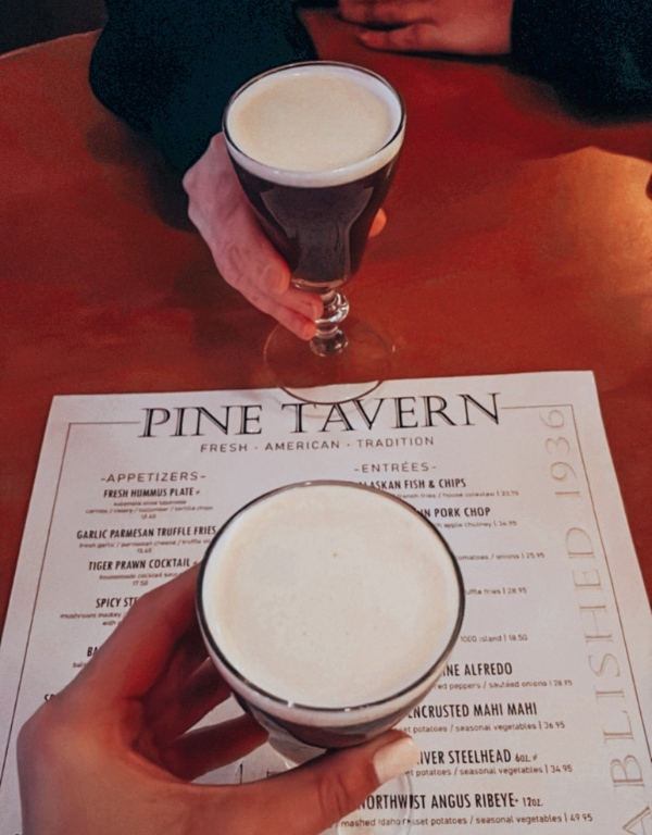 Two people are about to cheers their coffee over a menu that reads "Pine Tavern"