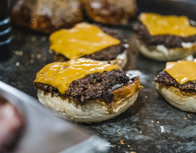 griddle with four burger buns topped with thinly pressed burgers and sliced cheese