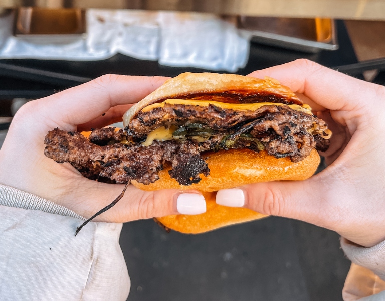 hands hold a smash burger with charred onions and cheese