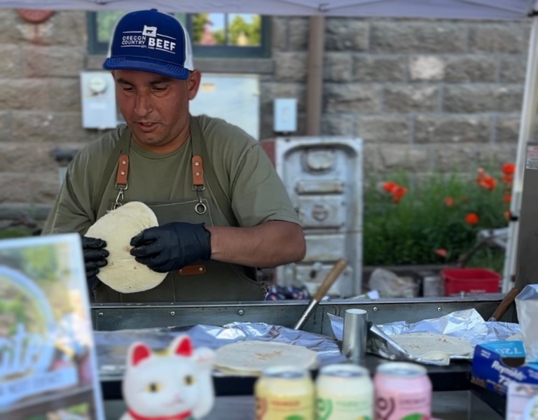 man holds a pita bread over a flat grill under a food cart
