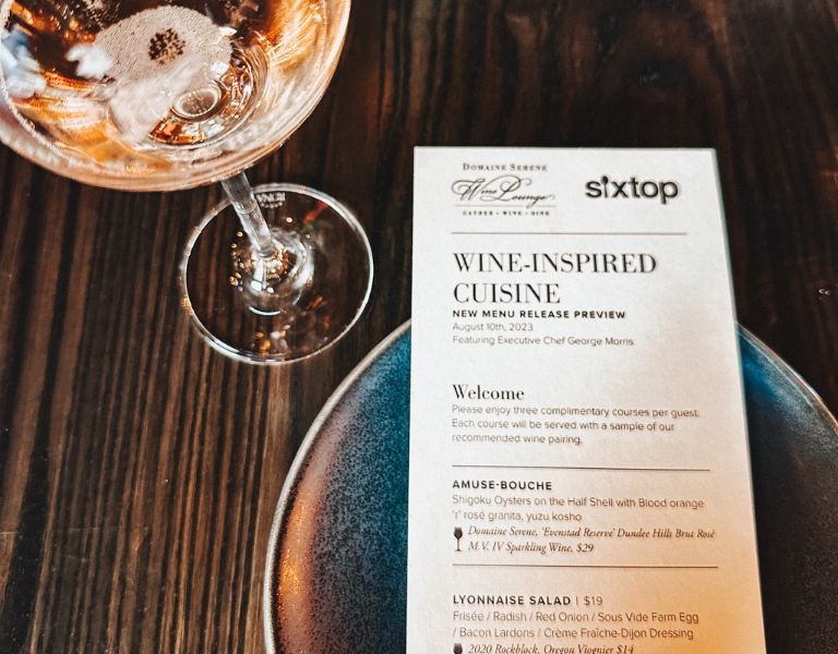 glass of sparkling domaine serene wine next to the menu