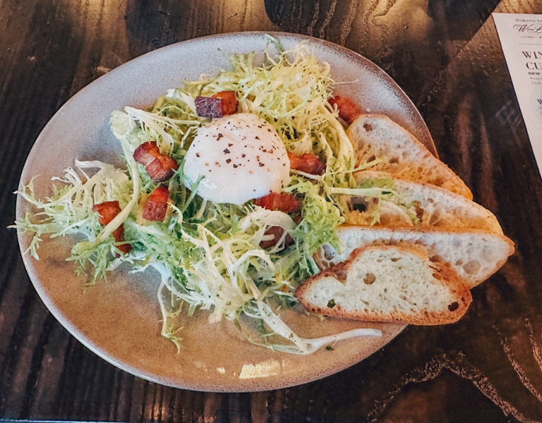 Lyonnaise salad topped with a poached egg and slices of grilled bread.