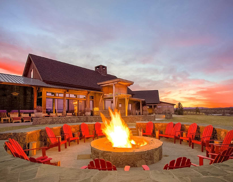 view of a circular fire pit lined with red adarondak chairs at brasada ranch